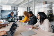 © Sergio Marcos/Stocksy - Group of multiracial businesspeople sitting around table having a remote video conference in modern workplace