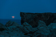 Full Moon Rising From Water Close To Cliffs