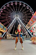 © Guaita Studio/Stocksy - Trendy woman standing in front of fair wheel holding a cotton candy