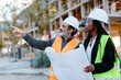© Jimena Roquero/Stocksy - Construction worker reporting to woman engineer while holding some blueprints in front of the construction.