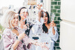 Pretty young women friends in bathrobes and pajama clink elegant glasses with delicious champagne at bachelorette party on hotel room terrace