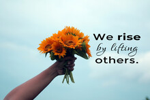 Inspirational Quote - We Rise By Lifting Others. Young Woman Showing Bouquet Of Sun Flowers In Hand Against Blue Sky Background. Positive Motivational Words Concept With Sunflowers.