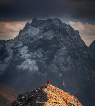 A Guy In A Red Jacket Stands On The Top Against The Background Of An Epic Mountain
