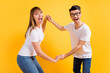 © deagreez - Photo of pretty excited young couple wear white t-shirt spectacles holding hands arms dancing isolated yellow color background
