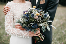 Close Up Of An Amazing Blue Wedding Bouquet And Bride And Groom Hugging