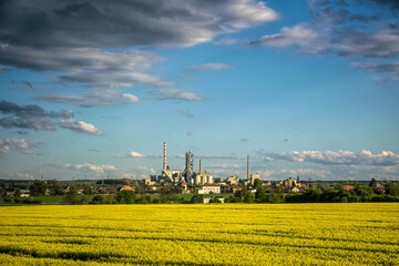 Canvas Print - Agricultural spring landscape in the Czech Republic. Sown rapeseed field and town houses and industrial buildings