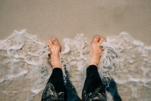 Looking Down At Feet Getting Wet By A Wave On A Sandy Beach