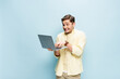 © LIGHTFIELD STUDIOS - happy young man in shirt typing on laptop isolated on blue