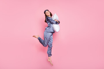 Wall Mural - Full length body size photo of girl wearing pajama hugging embracing pillow jumping isolated on pastel pink color background