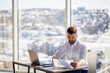 © Дмитрий Ткачук - An adult successful male businessman sits in his office with large windows and works at a laptop, working on new projects.