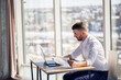 © DSMT - An adult successful male businessman sits in his office with large windows and works at a laptop, working on new projects.