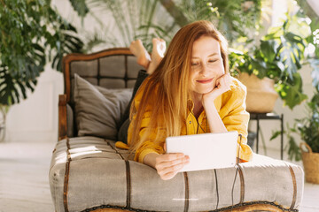 A beautiful woman sits at home among a large number of plants and communicates with relatives or friends using a tablet