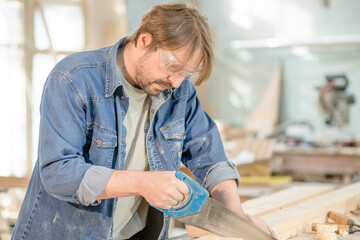 Wall Mural - Carpenter sawing a board with a hand wood saw in carpentry workshop