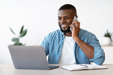 Wall Mural - Black Male Entrepreneur Talking On Cellphone And Working On Laptop In Office