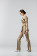 © LIGHTFIELD STUDIOS - full length of woman in stylish pantsuit standing on grey, side view