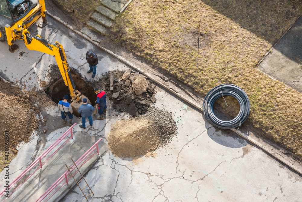 An excavator digs a trench to repair a pipeline on a city street Stock ...