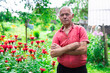 © caftor - elderly man in red shirt next to flower bed of Monarda didyma on garden plot in summer