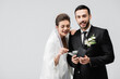 © LIGHTFIELD STUDIOS - Smiling bride looking at wallet with money in hands of muslim groom isolated on grey