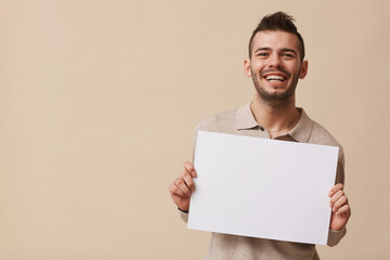 minimal waist up portrait of carefree young man holding blank white sign and smiling at camera while