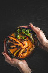 Poster - pan asian food. woman hands holding Tom Yam soup in black bowl on wooden table background