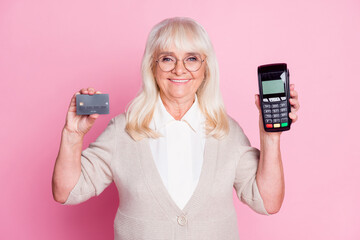 Wall Mural - Photo portrait of smiling woman holding credit card terminal in hands isolated on pastel pink colored background