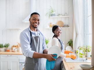 Happy black couple washing dishes together at kitchen, copy space. Family household duties concept