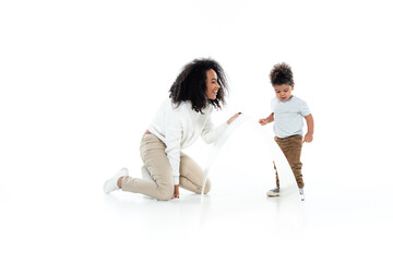 Wall Mural - full length view of cheerful african american woman and toddler son near paper roof on white