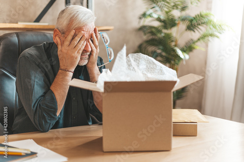 Damaged parcel box. Upset mature man closes his eyes, returns the goods to the store. A disgruntled online shopper. Broken item, delivery problem.
