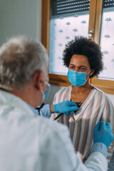 Wall Mural - Male doctor with face mask examining his female patient in clinic office