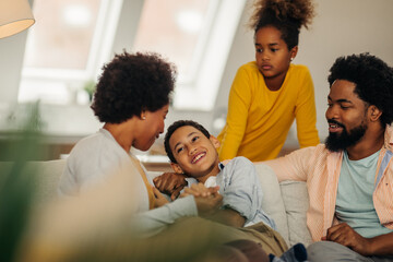 Wall Mural - Afro parents and their children are socializing while sitting on the sofa in the living room