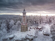 Aerial photo of Lookout tower Stepanka on the border of Krkonose and Jizera Mountains. Winter overcast day, sky with clouds, trees covered with snow.
