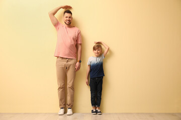 father and son comparing their heights near beige wall indoors. space for text