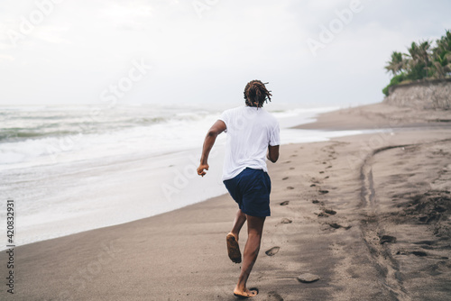Unrecognizable ethnic man running on empty seashore