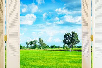 View through an open white wooden window onto green grass fields and blue sky.