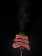Steak menu. Grilled hot pieces of beef steak medium rare with smoke on fork on black background.