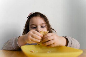 Toddler girl eating bread or pie at home with her hands. Hungry kid. Unhealthy diet. Bad table manners