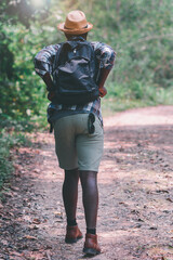 Wall Mural - African man traveler walking in the forest with backpack