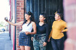 © Connect Images - Young woman and her teenage sisters posing for smartphone selfie in building entrance
