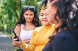 © Connect Images - Young woman with teenage sisters looking at smartphone by park, over shoulder view