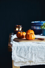 Still Life With Orange Pumpkins On Wooden Table With White Tablecloth And Black Background.