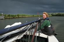 Woman Steers Sailing Boat With Lowered Mast Before Crossing Bridge, Friesland, Netherlands