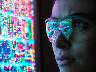 Electronic circuit board on computer monitor reflecting in glasses of a female engineer.