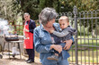 © Connect Images - Grandmother carrying baby boy at family BBQ gathering, Florence, Italy