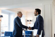 © Connect Images - Two businessmen standing indoors, shaking hands.