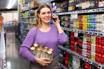 Wall Mural - Happy woman buys canned beer in hypermarket and talking on mobile phone