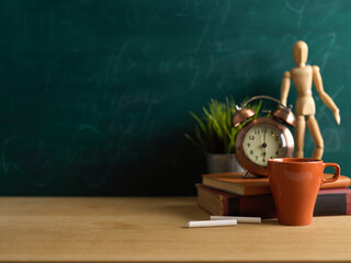 Wall Mural - Wooden table with books, mug, clock, decorations and copy space in classroom with chalkboard wall background