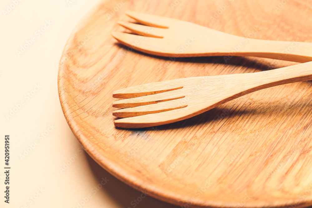 Wooden forks and plate on color background