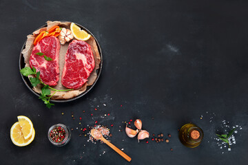 Wall Mural - Meat raw steaks with seasoning and herbs on dark background.