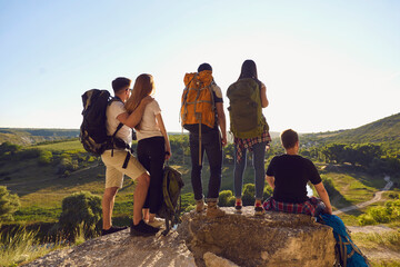 Wall Mural - group of tourists hikers standing and sitting and enjoying green valley landscape on summer vacation