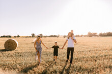 Happy Family Walks In The Field Near The Haystack At Sunset, Mom Dad And Two Sons, The Family Is Happy With Smiles On Their Faces, Hug The Children